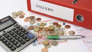 Steuern - Münzen, Aktenordner und Taschenrechner. | Bild: dpa/picture-alliance