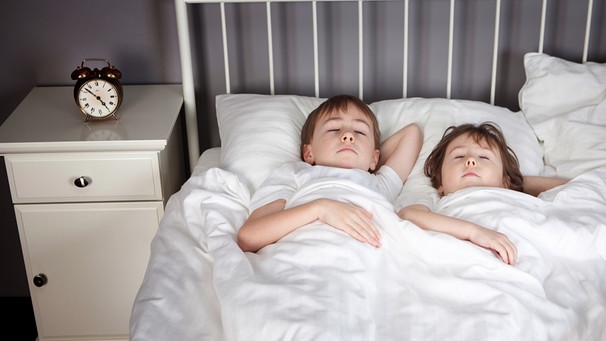 Kinder im Bett mit Wecker auf dem Nachttisch | Bild: picture-alliance/dpa