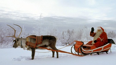 Der Weihnachtsmann auf seinem von einem Rentier gezogenen Schlitten im Schnee. | Bild: picture-alliance/dpa
