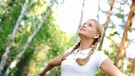 Eine junge Frau mit blonden Zöpfen steht im Wald und breitet die Arme aus. | Bild: colourbox.com