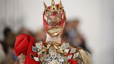 Eine Maske mit Perlenaugen und dreizackiger Krone | Bild: picture alliance / Photoshop