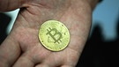 Ein Mann hält eine nachgemachte Münze mit dem Bitcoin-Logo in den Händen. Die Aussicht auf eine deutlich straffere Geldpolitik in den USA lastet zunehmend auf Digitalwährungen wie Bitcoin. | Bild: dpa-Bildfunk/Nicolas Armer