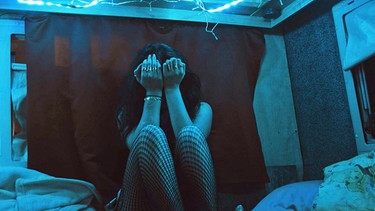 Szene aus dem Dokumentarfilm "Lovemobil": Eine Frau in einem schummrig beleuchteten Wohnmobil kauert auf einem Bett und verbirgt das Gesicht hinter ihren Händen | Bild: SWR/Christoph Rohrscheidt 