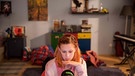 Eine junge Frau sitzt vor einem Computerbildschirm, in einem Zimmer, das aussieht wie ein Kinderzimmer | Bild: Hypermarket Film/Milan Jaroš