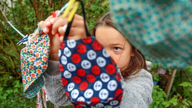 Ein kleines Mädchen hängt eine bunte Mundschutzmaske an eine Wäscheleine | Bild: BR Bild