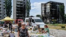 Bewohner der nordwestlich von der ukrainischen Hauptstadt Kiew gelegenen Stadt Borodyanka besuchen einen Markt in der Nähe von zerstörten Wohnhäusern, die von russischen Raketen getroffen wurden. Foto vom 7. Juli 2022.  | Bild: picture alliance / ZUMAPRESS.com | Sergei Chuzavkov