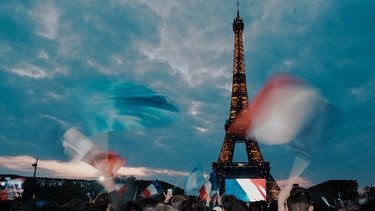 Anhänger des französischen Präsidenten Emmanuel Macron feiern unter düsterem Himmel am Eiffelturm mit Landesflaggen. | Bild: dpa-Bildfunk/Thibault Camus