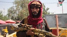Ein Taliban Kämpfer in Mehtarlam, Hauptstadt der Provinz Laghman im Osten Afghanistans, mit roten Tuch um Kopf und Hals, dunkel geschminkten Augenrändern, in der Hand ein Maschinengewähr in Tarnfarben. | Bild: picture alliance/dpa/Sputnik | Stringer