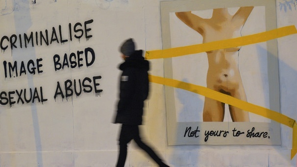 : Ein Mann läuft vor einem Graffity der irischen Künstlerin Emmalene Blake vorbei. An der Wand steht "Criminalise image based sexual abuse", daneben ist die Abbildung eines nackten Frauenkörpers mit der Unterschrift "Not yours to share" zu sehen. Dublin, November 2020. | Bild: picture-alliance/dpa Artur Widak/NurPhoto