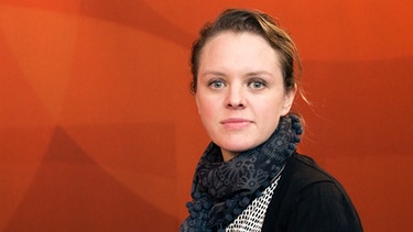Filmemacherin Julia von Heinz im Halbprofil vor einer orangefarbenen Wand | Bild: BR