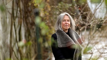 Die US-amerikanische Lyrikerin und Literaturnobelpreisträgerin Louise Glück steht hinter Zweigen eines Busches.  | Bild: dpa/Bildfunk_Daniel Ebersole
