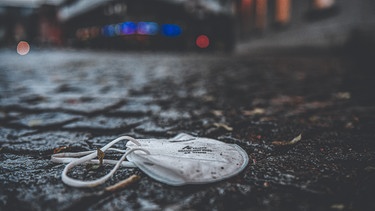 Eine verlorene oder achtlos weggeworfene, nasse Mund- und Nasenschutz-Maske auf dem Boden auf einem Pflasterstein. | Bild: picture alliance / Ostalb Network | Jason Tschepljakow
