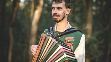 Musiker Maxi Pongratz steht mit einem Akkordeon im Freien und spielt | Bild: Christina Pichler