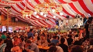 Menschen in Tracht in einem Bierzelt, im Hintergrund eine Band auf der Bühne: Das Würzburger Kiliani-Volksfest | Bild: picture alliance / imageBROKER | Martin Siepmann