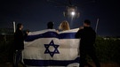 28.11.2023, Israel, Tel Aviv: Menschen, die eine israelische Flagge halten, beobachten die Ankunft eines Hubschraubers, der israelische Geiseln, die von der Hamas freigelassen wurden, zum Ichilov-Krankenhaus in Tel Aviv bringt. Die Hamas und Israel haben im Rahmen einer brüchigen Waffenruhe, die am Dienstag einen fünften Tag hielt, weitere Geiseln und Gefangene freigelassen. | Bild: dpa-Bildfunk/Leo Correa
