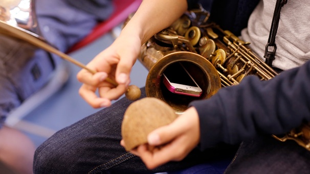 Schüler mit Saxophon und Percussioninstrumenten nimmt sich mit dem Smartphone auf. | Bild: BR