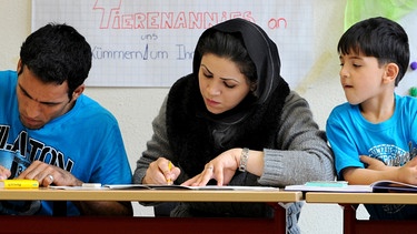 Deutsch als Fremdsprache, Eltern sitzen mit ihrem Sohn auf der Schulbank und lernen Deutsch.  | Bild: picture-alliance/dpa/Waltraud Grubitzsch