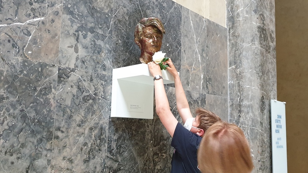 MünchenHören 2021: Ein Schüler legt eine weiße Rose vor der Bronzebüste von Sophie Scholl ab.  | Bild: BR | Judith Schönicke