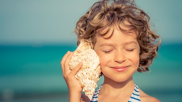 Ein Mädchen mit einer riesigen Muschel am Ohr. | Bild: iStock