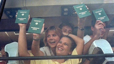 Glücklich halten Übersiedler aus der DDR, die am 11. September 1989 in einem Reisebus über Österreich in Bayern eintreffen, ihre bundesdeutschen Reisepässe in die Fensterscheibe des Busses. | Bild: picture-alliance/dpa