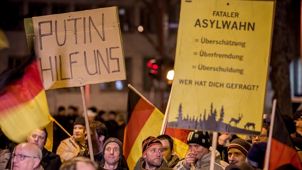 Unterstützer der Alternative für Deutschland (AfD) halten Schilder mit der Aufschrift "Putin hilf uns" und "Fataler Asylwahn" am 24.02.2016 bei einer Demonstration der AfD in Erfurt (Thüringen). | Bild: picture-alliance/dpa
