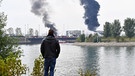 Passant steht vor dem Landeshafen Nord und blickt auf die Rauchsäulen | Bild: picture-alliance/dpa
