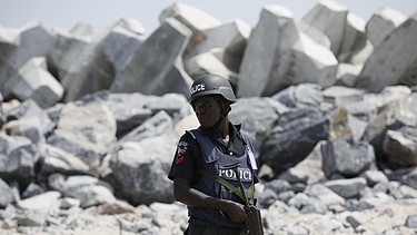 Ein nigerianischer Polizist vor einem Wall der entstehenden Eko Atlantic City in Lagos | Bild: picture-alliance/dpa/Kristin Palitza