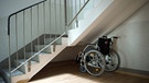 in Rollstuhl steht unter einer Treppe in einem Wohnhaus in Weißwasser (Sachsen).  | Bild: picture-alliance/dpa