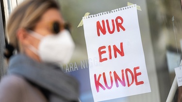 ARCHIV - 26.04.2020, Bayern, München: Eine Frau mit Nase-Mund-Schutzmaske geht an einem Geschäft vorbei, an dem ein Schild mit der Aufschrift "Nur ein Kunde" angebracht ist. Auch wenn sich täglich noch Menschen in Bayern an dem neuartigen Coronavirus infizieren, drosselt die Staatsregierung die Gegenmaßnahmen wieder ein wenig herunter. Foto: Peter Kneffel/dpa +++ dpa-Bildfunk +++ | Bild: dpa-Bildfunk/Peter Kneffel
