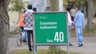  Flüchtlinge halten sich in München (Bayern) in der Erstaufnahmeeinrichtung für Asylbewerber auf dem Gelände der Bayernkaserne im Freien hinter einem Schild auf | Bild: picture-alliance/dpa