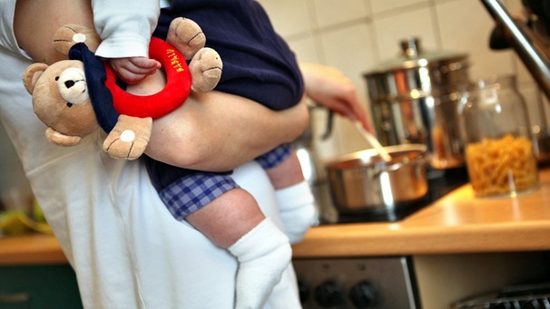 Mutter mit Kleinkind auf dem Arm kocht | Bild: picture-alliance/dpa