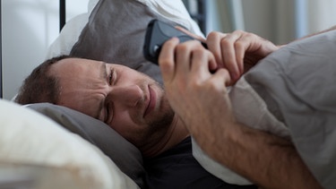 Ein Mann nutzt sein Smartphone, waehrend er im Bett liegt | Bild: picture-alliance/dpa/Christin Klose
