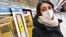 Eine junge Frau mit FFP2-Maske steht vor einem U-Bahn-Waggon in München. | Bild: picture alliance / SvenSimon | Frank Hoermann/SVEN SIMON