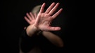 Foto: Hintergrund dunkel, vorne streckt eine weiblich gelesene Person ihre Hände zum Schutz aus | Bild: IMAGO/Pixsell