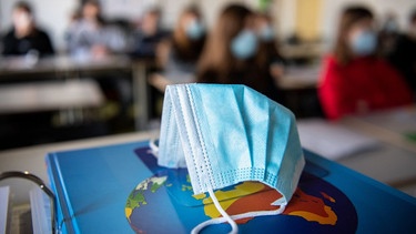 Eine Maske auf einem Weltatlas in einem Klassenzimmer mit Präsenzunterricht | Bild: dpa-Bildfunk/Matthias Balk