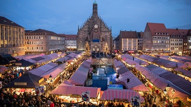 Viele Menschen drängen sich in den hell erleuchteten Budengassen des Nürnberger Christkindlesmarktes.  | Bild: dpa/ Daniel Karmann