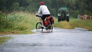 Archivbild: Ein Radfahrer ist im Regen auf einem überfluteten Radwanderweg an der Donau unterwegs. (Archivbild) | Bild: picture alliance/dpa | Thomas Warnack