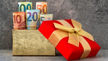Ein verpacktes Geschenk, dahinter ein Goldenes Kästchen aus dem Geldscheine herausschauen | Bild: picture alliance/Zoonar/Grazvydas Januska