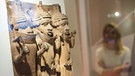 Besucherin betrachtet Skulptur mit drei Figuren in einer Vitrine | Bild: Daniel Bockwoldt/Picture Alliance