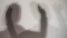 Symbolbild: Silhouette von zwei Menschen mit hochgestreckten Händen hinter einer trüben Scheibe. | Bild: picture alliance