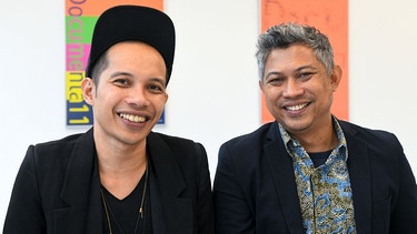 Zwei Mitglieder des indonesischen Künstlerkollektivs Ruangrupa lächeln in die Kamera - vor der documenta fifteen. | Bild: dpa/Bildfunk