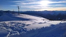 Ein kleines vertikales Windrad steht südlich vom Rotwandhaus im Mangfallgebirge im tiefen Schnee. Dahinter das Alpenpanorama, darüber blauer Himmel mit leichter Bewölkung. | Bild: BR/ Thomas Reichart
