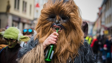 Ein als Chewbacca verkleideter Besucher eines Faschingsumzugs trinkt Bier. | Bild: picture alliance / Nicolas Armer/dpa | Nicolas Armer