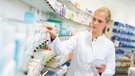 Eine Apothekerin vor Medikamenten in der Auslage.  | Bild: stock.adobe.com/benjaminnolte