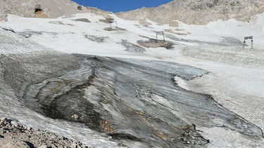Schneereste auf felsigem Untergrund - vorne  schwarzgrauer Gletscher, dahinter Liftstützen des Skigebiets auf der Zugspitze | Bild: picture-alliance /dpa/ Angelika Warmuth