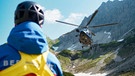 Ein Hubschrauber landet in den Bergen, während ein Bergretter von der Bergwacht Allgäu am Boden wartet. | Bild: BR/Luis Trautmann