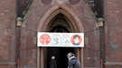 Ein Banner mit Informationen zum Schutz vor Corona-Infektionen hängt über dem Eingangsportal einer Kirche.  | Bild: Caroline Seidel/dpa-Bildfunk