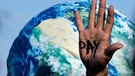 Auf einer Hand ist "Pay" zu lesen, dahinter ist die Erdkugel abgebildet | Bild: dpa-Bildfunk/Peter Dejong