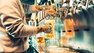 Junger Barkeeper steht am Zapfhahn um Biergläser zu füllen. | Bild: stock.adobe.com/master1305