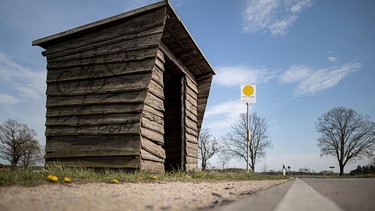 Eine Holzhütte steht als Bushaltehäuschen an einer Landstrasse. | Bild: picture alliance / photothek | Florian Gaertner